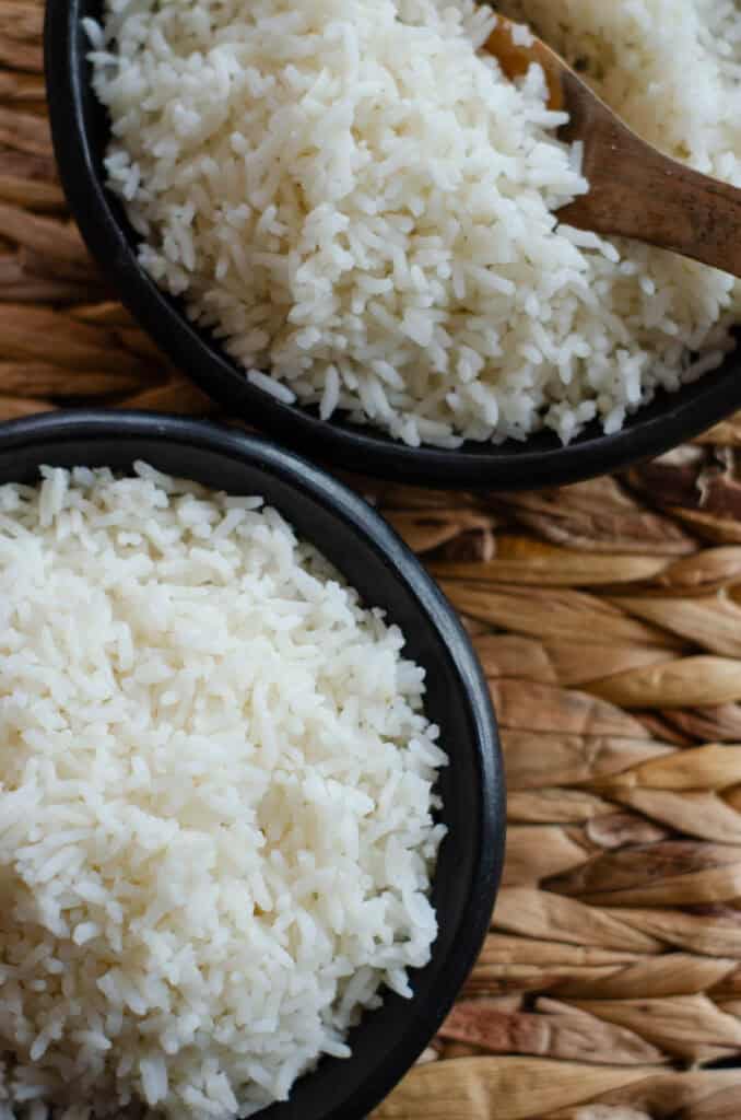 shot from above of two black bowls containing white rice, one has a wooden spoon in it