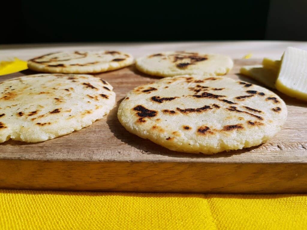 4 Arepas Colombianas (Colombian Corn Cakes) on a cutting board with cheese next to it
