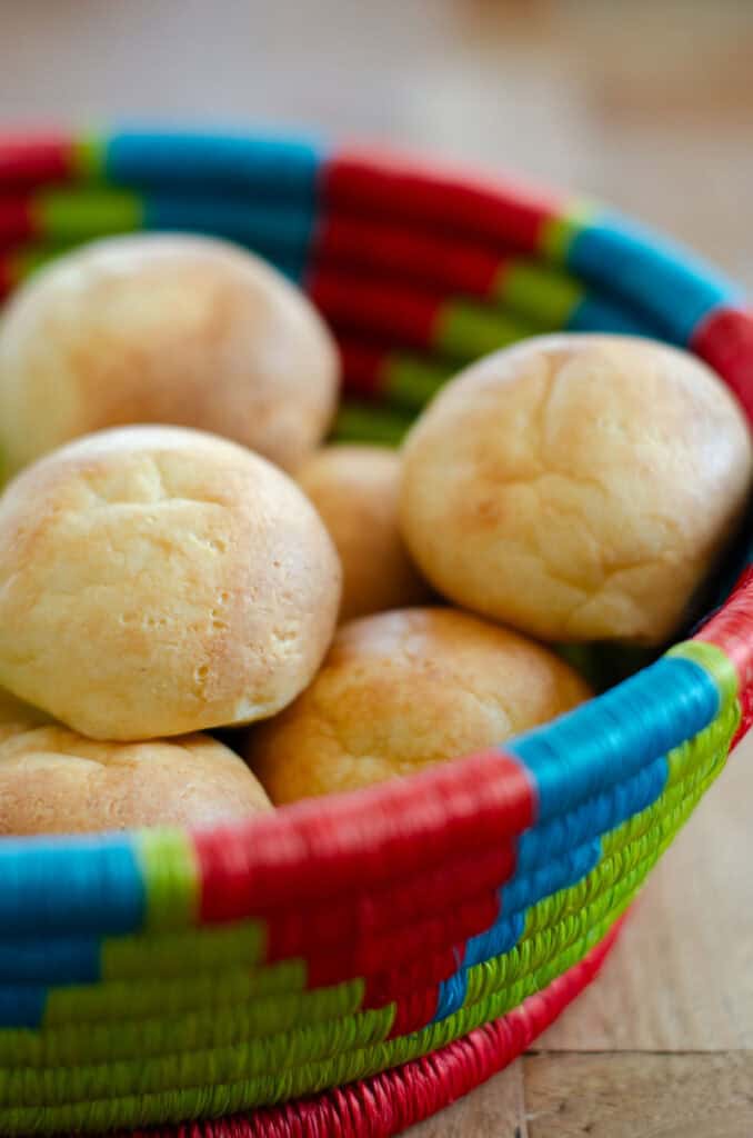 close up picture of a couple of golden brown homemade almojabanas in a traditional colombian colorful bread basket