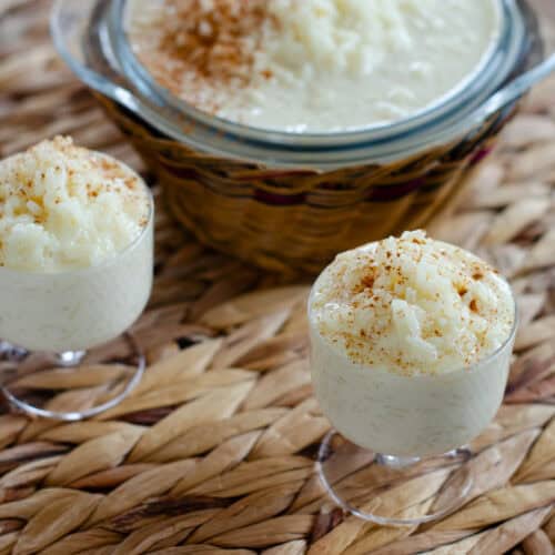 dos vasitos con un cremoso arroz con leche y al fondo un bol grande con arroz con leche y canela