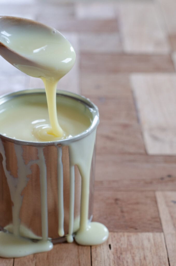can with condensed milk and condensed milk dripping from a spoon