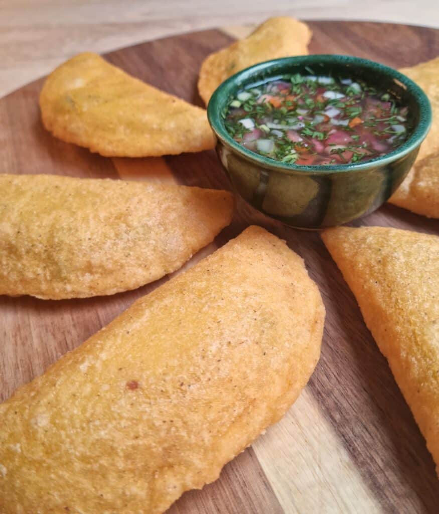 Colombian Vegan Empanadas on a serving board with a bowl of aji picante in the middle
