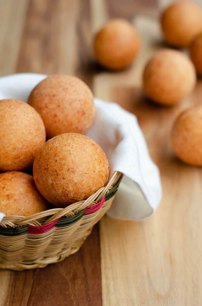 Colombian Buñuelos in a traditional basket on a wooden table, with some bunuelos in the background