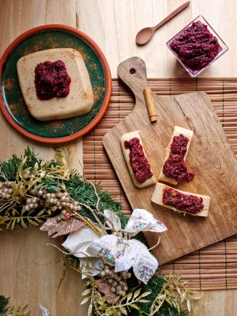 top shot of colombian natilla custard pudding on a plate, a cutting board with pieces of natilla, blackberry sauce and christmas decoration