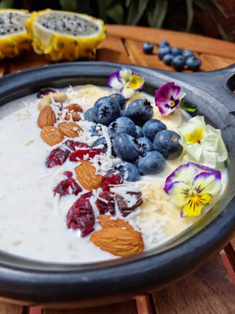 Black bowl with the breakfast fariña with milk, fruits, nuts and flowers for decoration