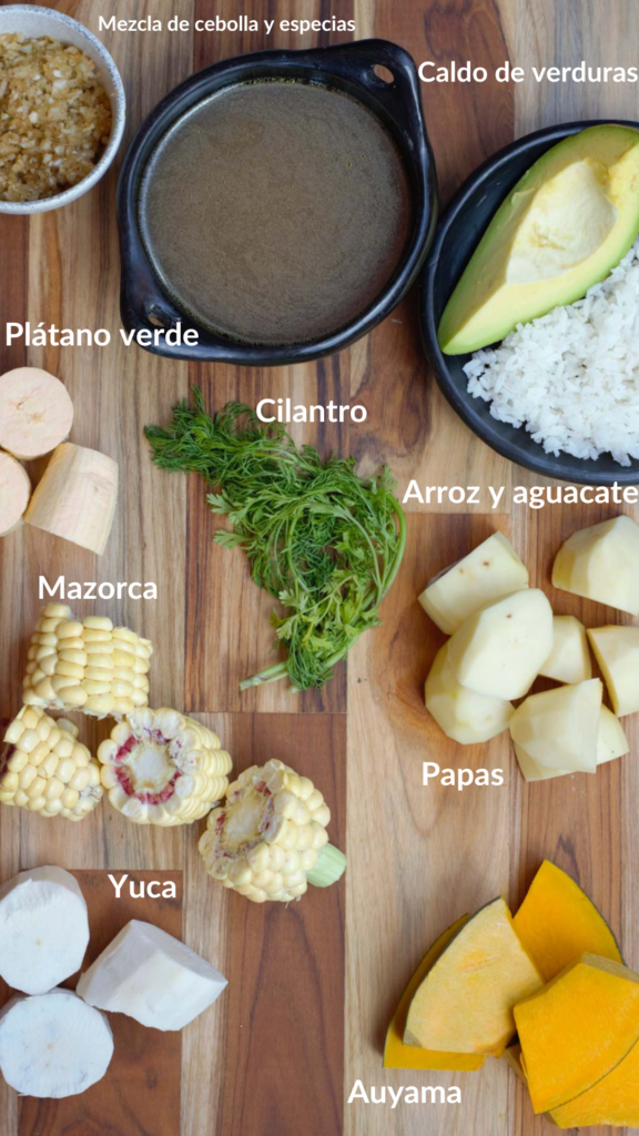 Todos los ingredientes del sancocho en una tabla para cortar: mezcla de cebolla y especias, caldo de verduras, arroz, aguacate, cilantro, plátano verde, papa, mazorca, yuca y auyama