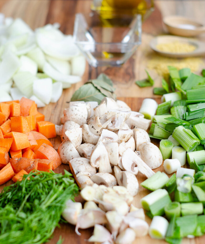 en una tabla todos los ingredientes del caldo: cebolla, zanahoria, cilantro, champinones, ajo, puerro, levadura nutricional, sal, aceite y vinagre
