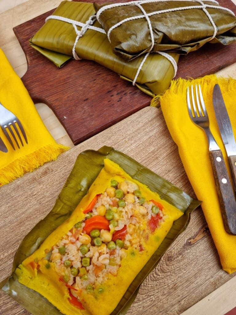 One open tamal on a cutting board with two still wrapped tamales in the background