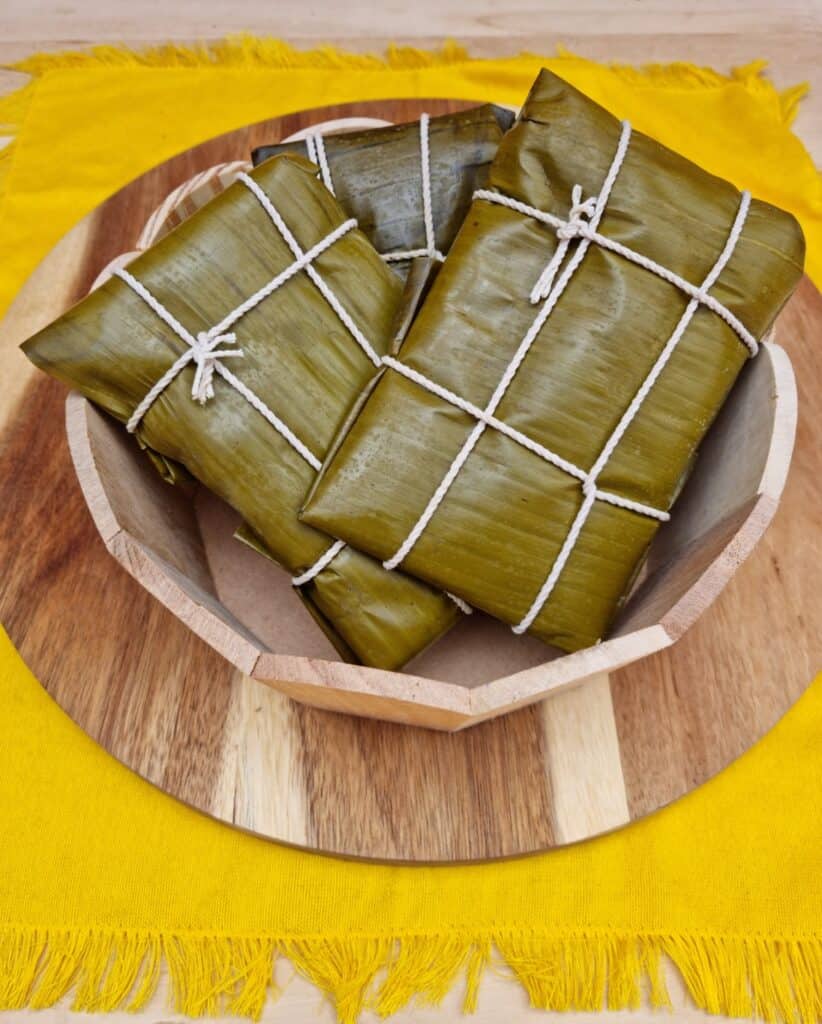 Three vegan colombian tamales still wrapped in plantain leave in a basket