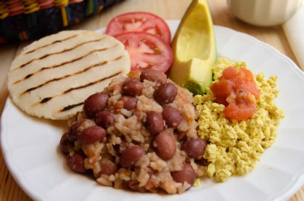 Colombian Vegan Breakfast Calentado on a plate with rice and beans, tofu scramble, avocado, tomato and arepa