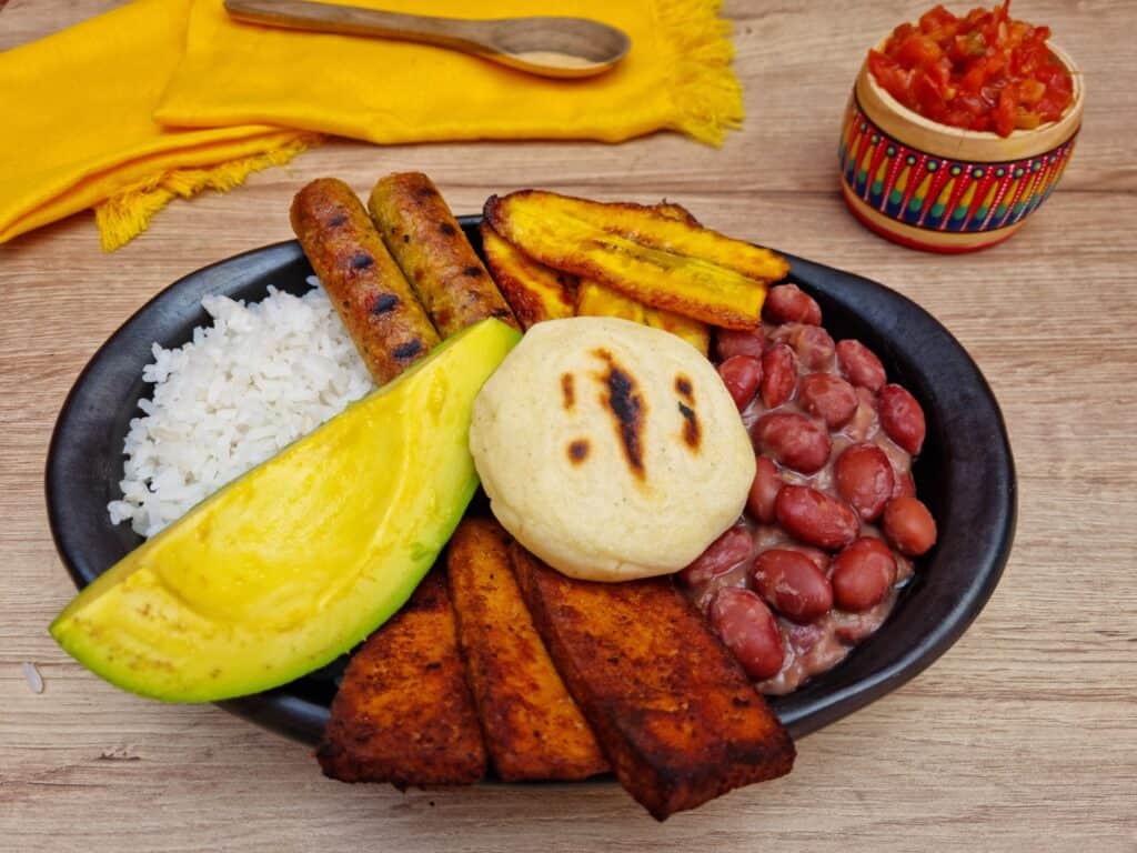 Traditional plate with beans, plantain, arepa, vegan sausage, bbq tofu, rice and avocado. 