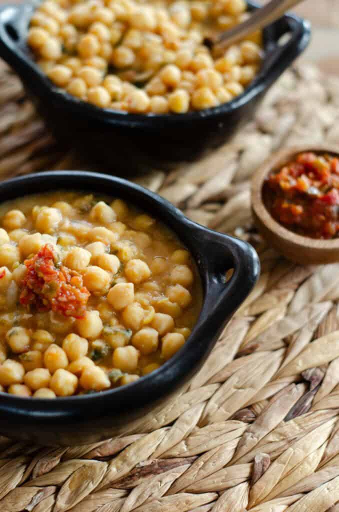 dos platos negros con garbanzos colombianos en guiso y un vasito con hogao