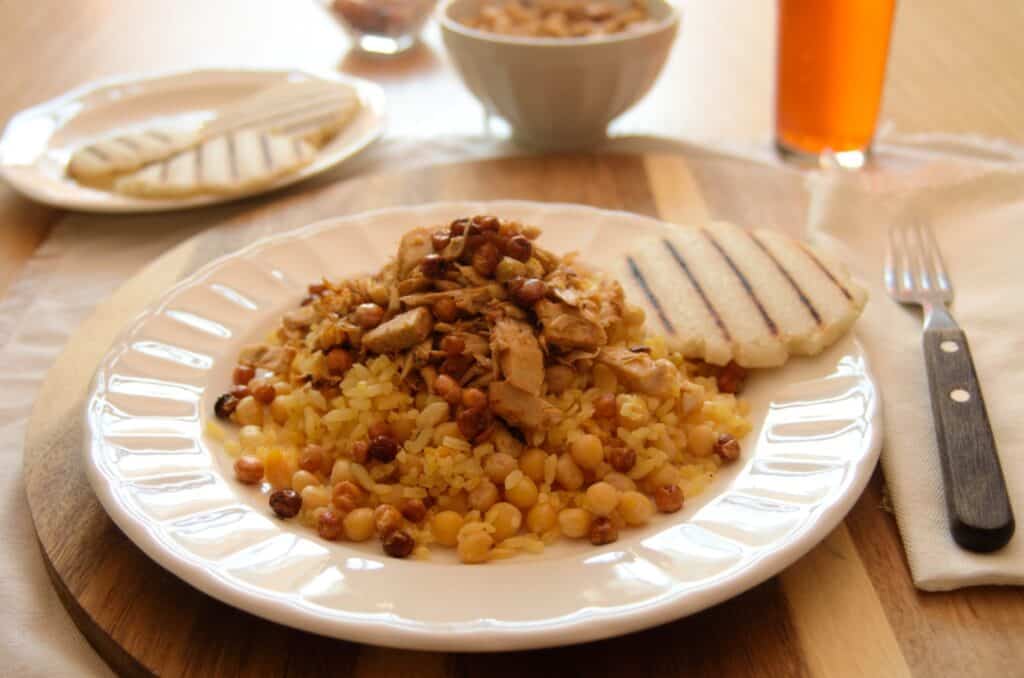 Plato con lechona de yaca con arvejas crujientes, arepa blanca y gaseosa al fondo