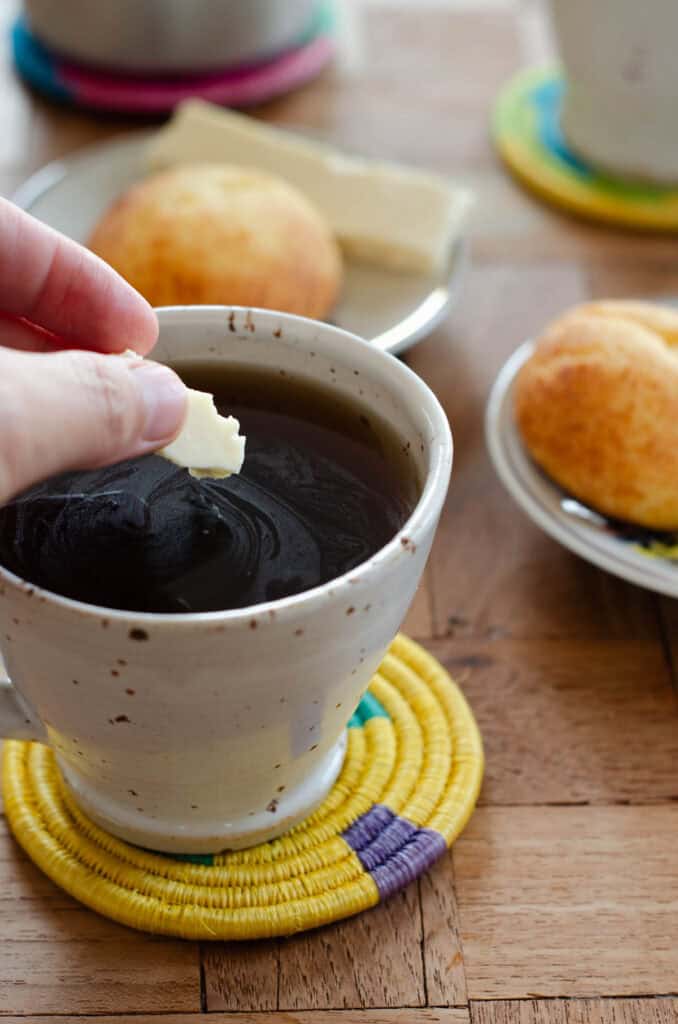 a hand holding a piece of cheese over a cup of aguapanela