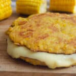 arepa de choclo on a wooden cutting board with corn in the background