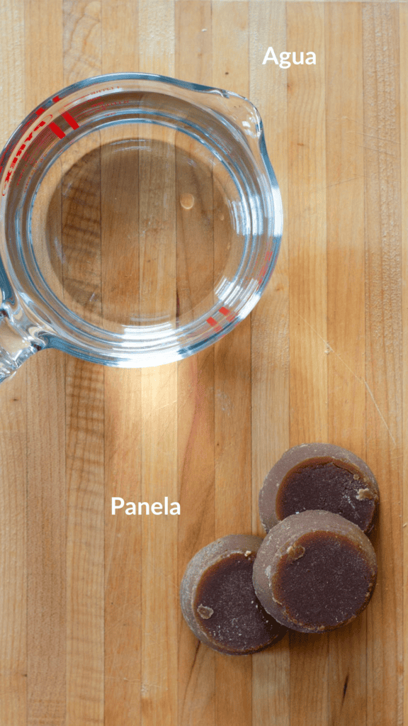 Foto con los ingredientes: una taza de agua y tres bloques de panela en una tabla de madera
