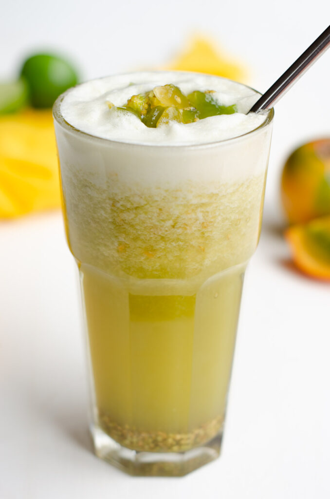 lulada in glass with chunks of lulo on top and in the background a yellow napkin, lime and lulo