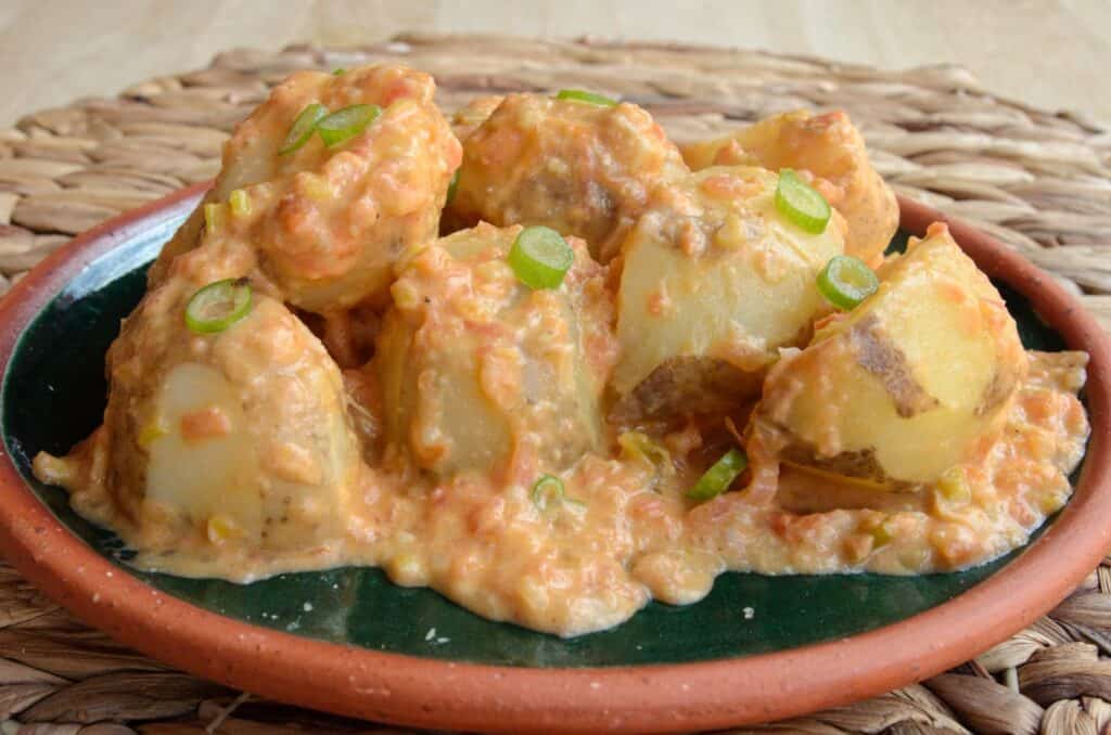 Plato verde con papas banadas en la salsa de tomate, crema y queso