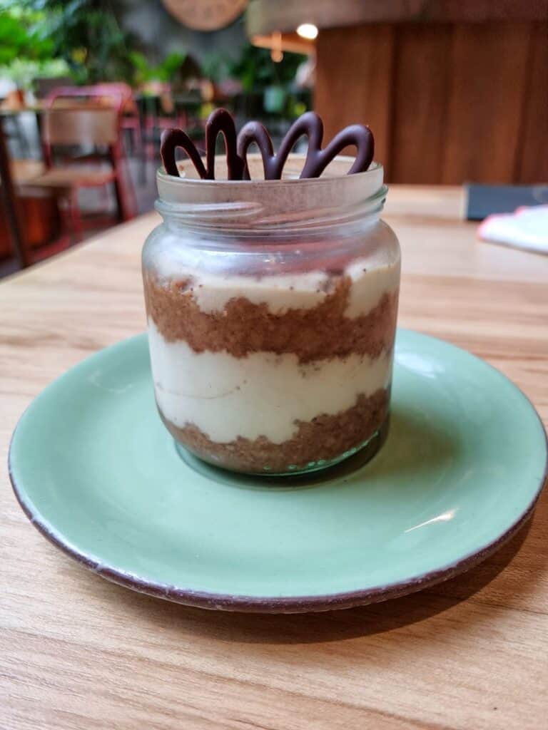Glass jar with vegan tiramisu on a blue plate and a wooden table