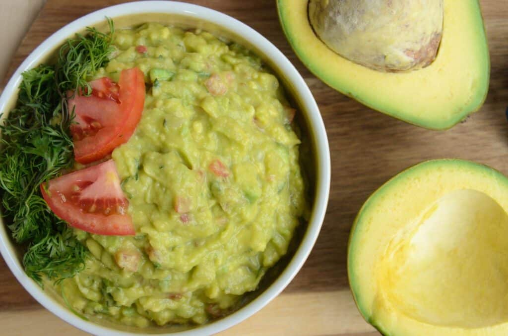 Guacamole in a bowl viewed from above with two avocado halves next to it