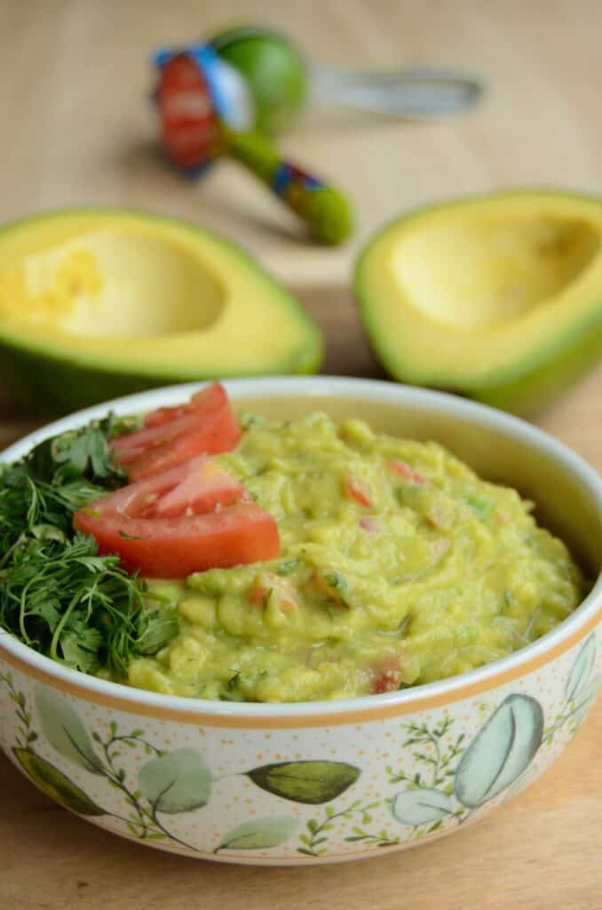 guacamole in a flowered bowl with avocados in de background