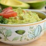 bowl with guacamole, a lime squeezer and avocado in the background