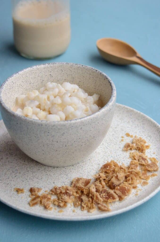 cup with hominy and a plate with grated panela. A glass milk bottle and a wooden spoon in the background