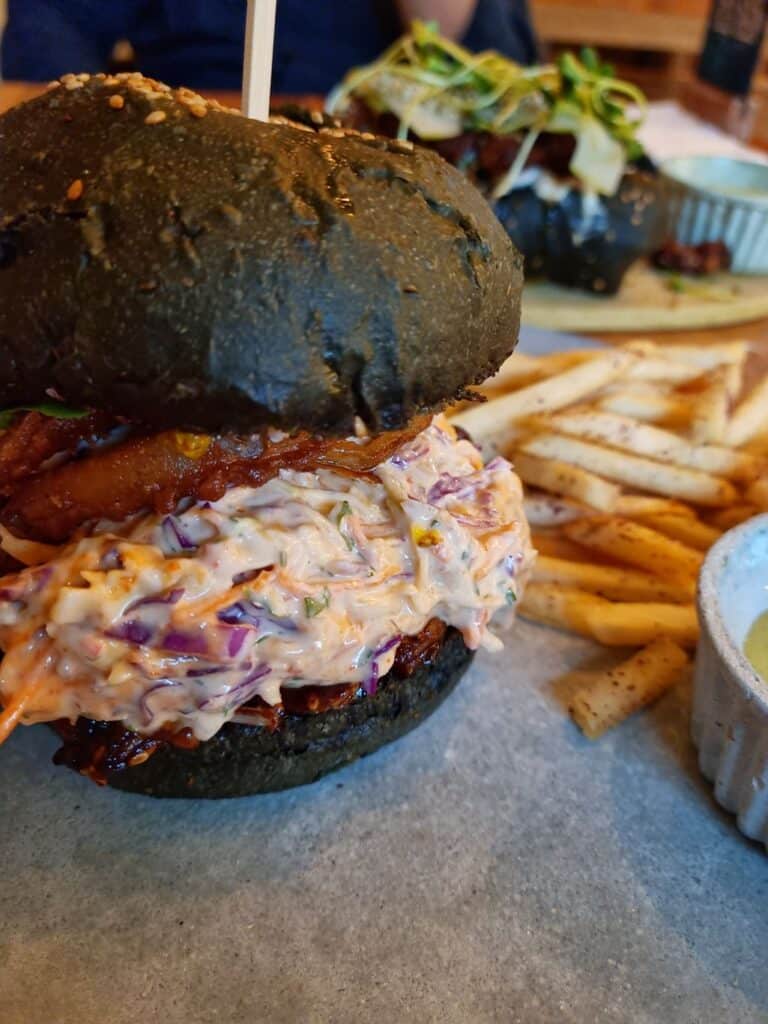 Burger with coleslaw and fries on a table with a hot dog in the background