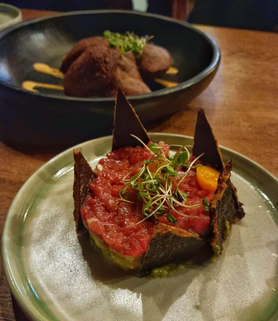 Watermelon steak tartare on a green plate with another dish in the background