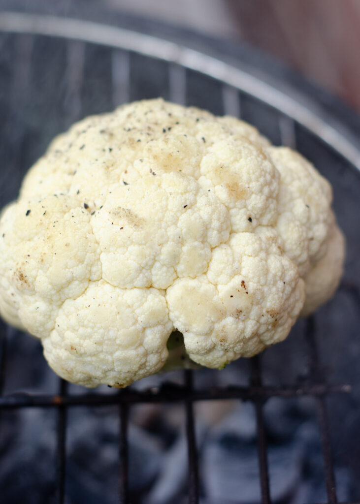 raw cauliflower just placed on the BBQ grill