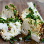 Chunks of grilled cauliflower with dollops of chimichurri on a cutting board
