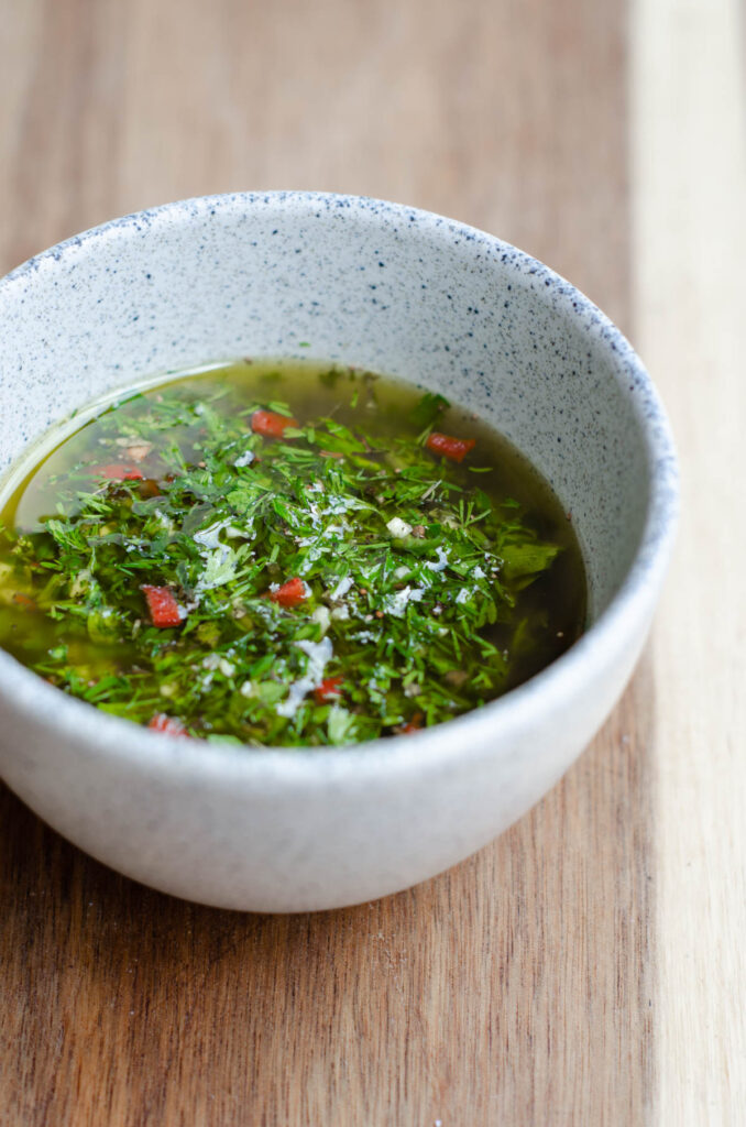 light colored bowl with chimichurri on a wooden cutting board