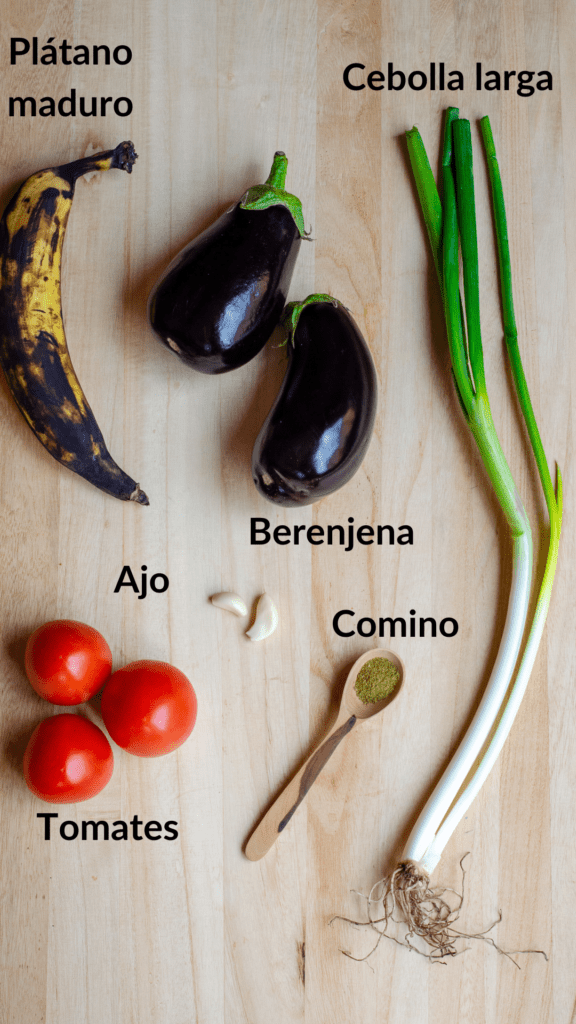 plátano maduro, berenjena, cebolla larga, ajo, comino y tomate en una mesa de madera