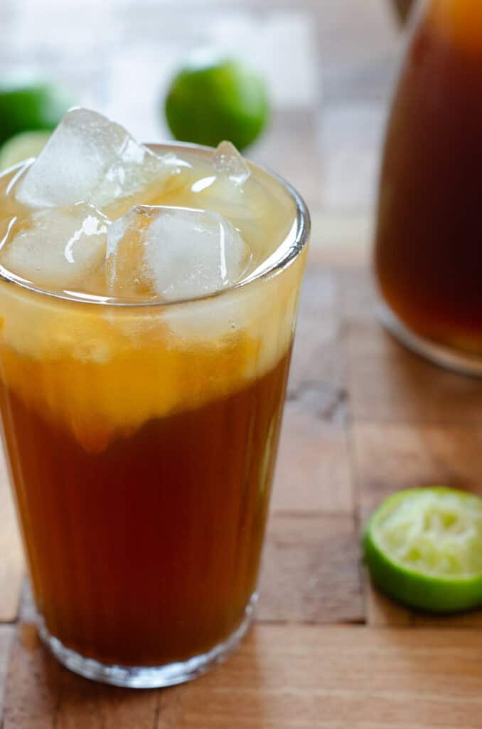 glass with limonada de panela, ice cubes, lime, and in the background a pitcher with the limeade, and limes