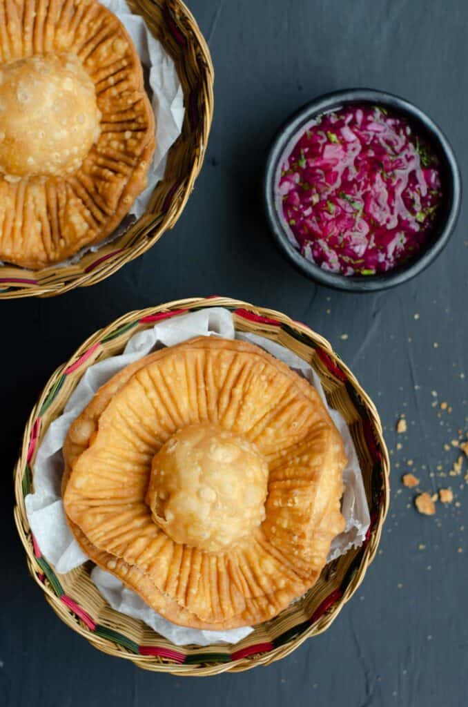 top shot of two baskets with fried chickpea pasties and a bowl of pickled red onion salsa
