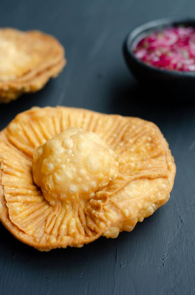close up of one chickpea pasty with another one in the back together with a bowl of pickled red onion salsa