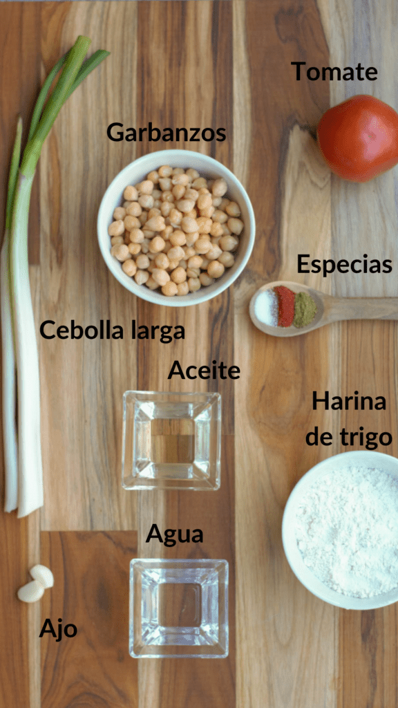 los ingredientes de los pasteles de garbanzo en una tabla para cortar: garbanzos, cebolla larga, ajo, tomate, especias, harina de trigo, agua y aceite