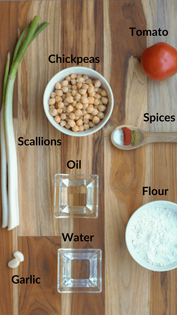 ingredients of chickpea pasties on a cutting board: scallions, chickpeas, tomato, spices, garlic, flour, water, oil