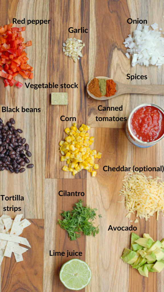 Cutting board with all the ingredients for the tortilla soup: onion, garlic, red pepper, tomatoes, spices, vegetable stock, black beans, corn, tortilla strips, cilantro, lime juice, cheese, cheddar