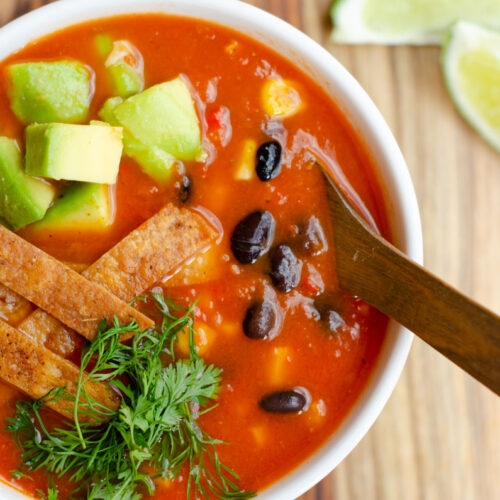 bol con la sopa de tomato, cubierta con frijoles negros, maiz, aguacate, tiras de tortilla, cilantro