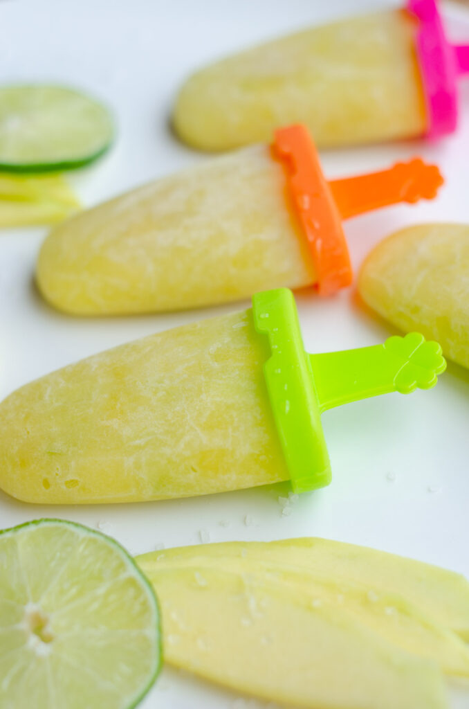 white plate with green mango popsicles lined up, decorated with green mango, lime and salt