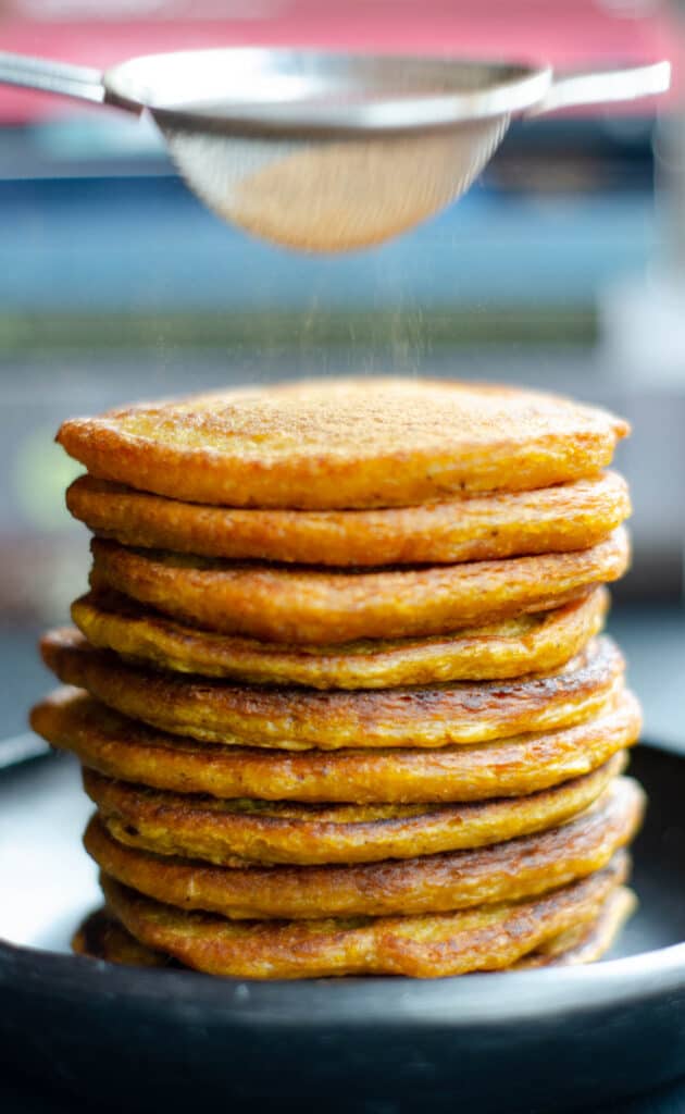 stack of pumpkin pancakes with a cinnamon being sifted ovet them