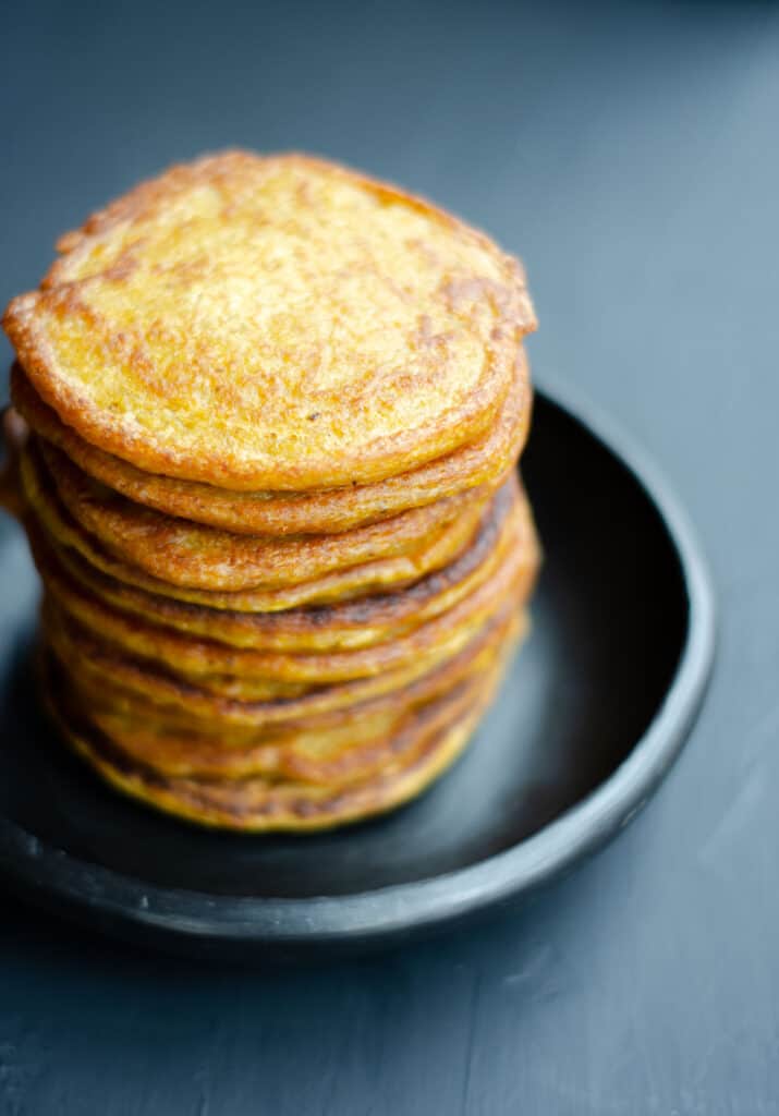 in a black bowl a high stack of pumpkin pancakes against a dark background