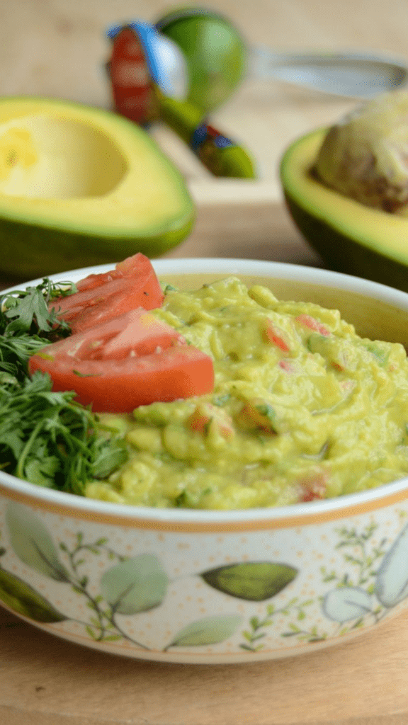 bowl of guacamole decorated with cilantro and tomato, with avocados in the background