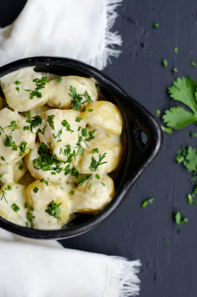 top shot of the bowl with boiled potatoes in cream sauce, scattered green herbs and a white kitchen towel