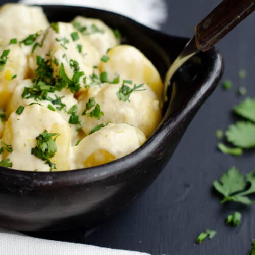 black bowl with potatoes in milk cream sauce, sprinkled with green herbs and a white kitchen towel