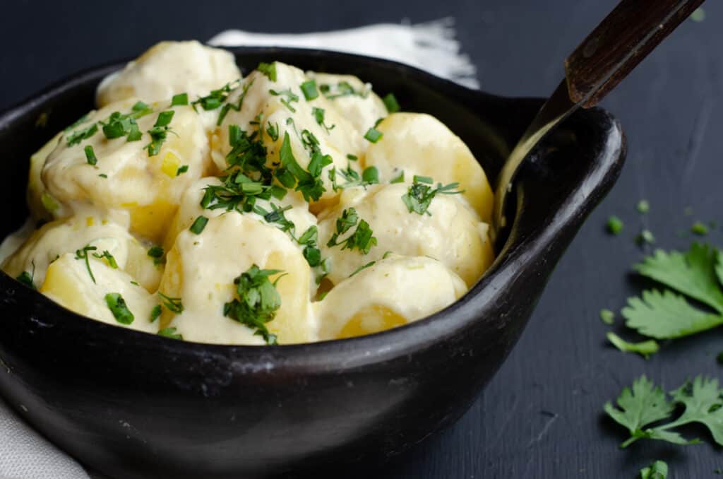 black bowl with potatoes in milk cream sauce with green herbs around