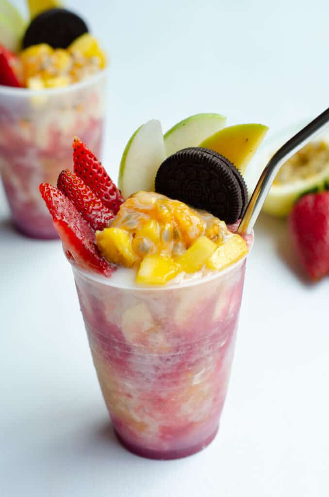 hielo raspado con almibares de fruta, banano, mango, fresa, manzana, maracuya, galleta oreo y leche condensada en una copa de plastico con pitillo