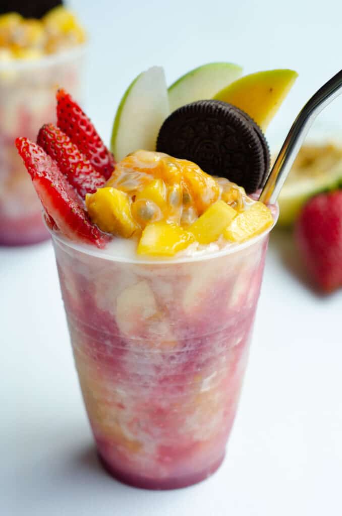 plastic cup with shaved ice and fruit syrup, topped with mango, banana, strawberry, passion fruit, green apple, oreo cookie and condensed milk