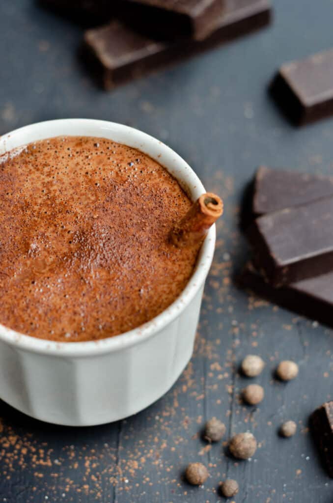 cup of hot chocolate with spices and chocolate bars around it, and cocoa powder sprinkled around